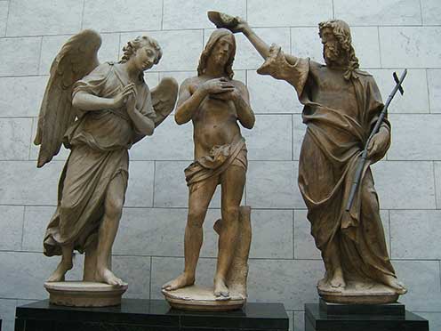 Three white marble statues on black marble pedestals representing Jesus being baptized by John the Baptist, with an angel looking on.
